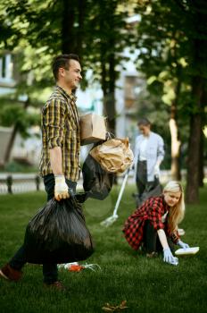 Young man holds plastic trash bags in park, volunteering. Male person cleans forest, ecological restoration, eco lifestyle, garbage collection and recycling