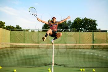 Happy male tennis player jumps with racket at the net on outdoor court. Active healthy lifestyle, sport game competition, fitness training with racquet