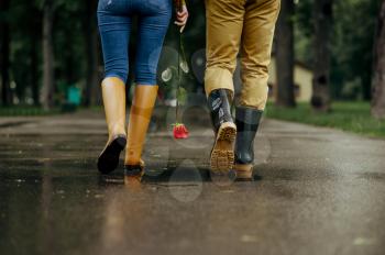Love couple walks in park, summer rainy day. Man and woman leisures together, romantic date on walking path, wet weather in alley