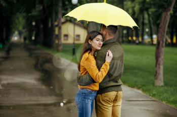Love couple hugs in park, summer rainy day. Man and woman stand under umbrella, romantic date on walking path, wet weather in alley