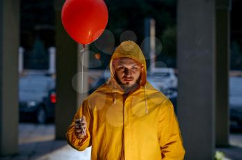Scary man with balloon walking in night summer park in rainy day. Strange male person in rain cape, wet weather in alley