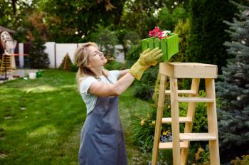 Happy woman looks on flower bed in the garden. Female gardener takes care of plants outdoor, gardening hobby, florist lifestyle and leisure