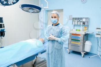 Female surgeon in gown, mask and gloves in operating room, patient on surgery operation. Doctor in uniform, medical clinic worker, medicine and health, healthcare in hospital
