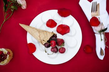 Table setting, tea party, waffle cone with fresh berries, top view, nobody. Luxury silverware on red tablecloth, tableware outdoors. Wedding celebration on summer meadow