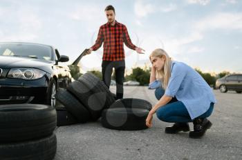 Sad female student against downed tires, lesson in driving school. Man teaching lady to drive vehicle. Driver's license education, instructor and woman