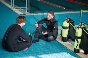 Two divers in scuba gear leisures after dive lesson in diving school. Teaching people to swim underwater, indoor swimming pool interior on background