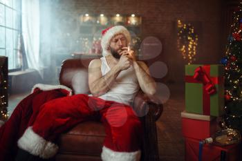 Bad Santa claus smoking cigar on sofa, nasty party, humor. Unhealthy lifestyle, bearded man in holiday costume, new year and alcoholism