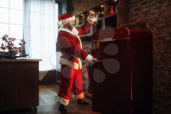 Bad impudent Santa claus steals alcohol from refrigerator, nasty party, humor. Unhealthy lifestyle, bearded man in holiday costume, new year and alcoholism