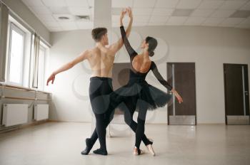 Female and male ballet dancers, dancing in action. Ballerina with partner training in class, dance studio interior on background