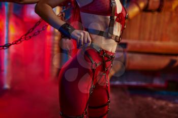 Sexy woman body in red bdsm suit chained up, abandoned factory interior on background. Young girl in erotic underwear, sex fetish, sexual fantasy