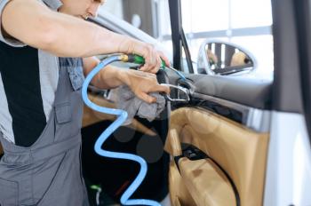 Worker removes dirt with air, car dry cleaning and detailing. Vehicle washing in garage, thoroughly care of automobile, chemical and vacuum clean service