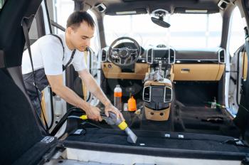 Worker cleans car interior trim with vacuum cleaner, car dry cleaning and detailing. Vehicle washing service in garage, thoroughly care of automobile