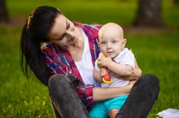 Portrait of mother and her little baby are sitting on the grass in summer park. Mom with male kid leisures on lawn, picnic with child on plaid in the forest, family on vacations