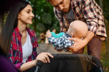 Caring parents with little baby walking in summer park. Mom and dad leisures with male kid, picnic with child in the forest, family happiness