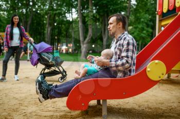 Happy parents play with little baby on playground in summer park. Mom and dad leisures with male kid, picnic with child in the forest, family happiness