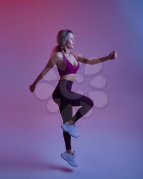 Young woman with slim body poses in studio, neon background. Sportswoman at the photo shoot, sport concept, active lifestyle motivation
