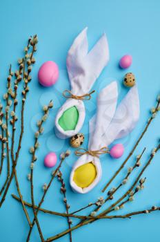 Colorful easter eggs and willow branch on blue background, top view. Paschal food, event decoration, spring holiday celebration, traditional symbol