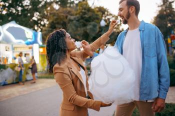 Love couple eating cotton candy in city amusement park. Man and woman relax outdoors. Family leisures in summertime, entertainment theme