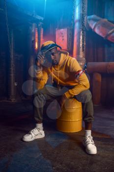 Rapper in yellow hoodie poses in studio with cool underground decoration. Hip-hop performer, rap singer, break-dance
