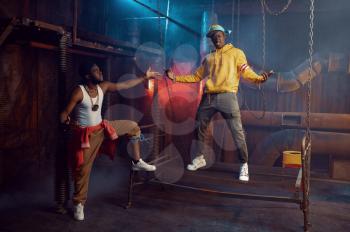 Two rappers posing, performing in cool studio, underground decoration. Hip-hop performers, trendy rap singers, break-dancers