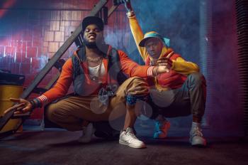 Two serious rappers with gold jewelry poses in cool studio, underground decoration. Hip-hop performers, trendy rap singers, break-dancers