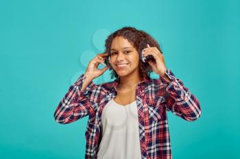 Cute young woman in headphones, blue background, positive emotion. Face expression, female person looking on camera in studio, emotional concept, feelings