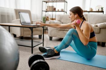 Girl sitting at the laptop, online fit training. Female person in sportswear, internet sport workout, room interior on background