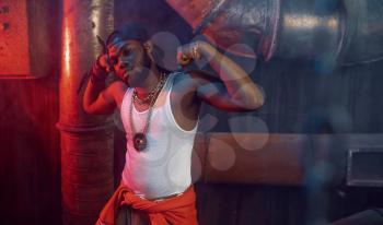 Stylish rapper shows his muscles in studio with cool underground decoration. Hip-hop performer, rap singer, break-dance