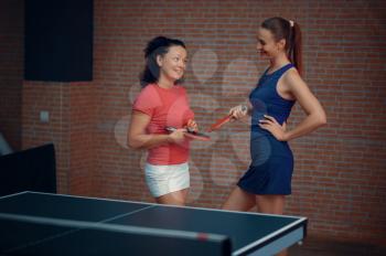 Women play doubles table tennis, ping pong players. Friends playing table-tennis indoors, sport game with racket and ball, active healthy lifestyle