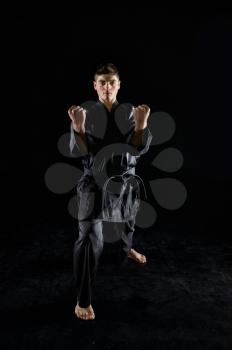 Male karate fighter in black kimono, combat stance, front view, dark background. Man on workout, martial arts, fighting competition