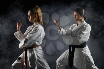 Female karatekas, training in white kimono, combat stance in action, dark background. Karate fighters on workout, martial arts, women fighting competition