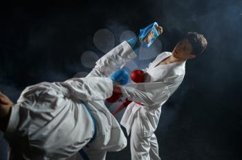 Two male karatekas in white kimono and gloves, combat in action, dark background. Fighters on workout, martial arts, fighting competition
