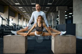 Slim couple doing stretching exercise on cubes in gym. Athletic man and woman on workout in sport club, active healthy lifestyle, physical wellness