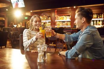 Man and woman drinks alcohol and talking at the table in bar. Group of people relax in pub, night lifestyle, friendship, event celebration