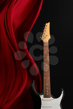 Black electric guitar, red curtain, black background, nobody. String musical instrument concept, electro sound, electronic music, equipment for stage concert