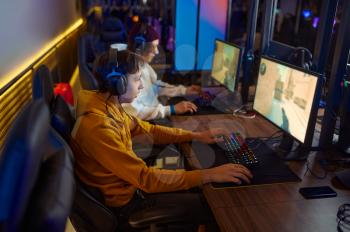 Two young gamers in headsets play in video game club. Virtual entertainment, e-sport tournament, cybersport lifestyle. Male person leisures in internet cafe