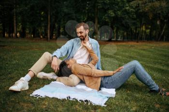 Smiling love couple resting on the grass, top view, romantic walking in the park. Man and woman lying on a blanket. Family relax on the meadow in summertime, weekend in nature