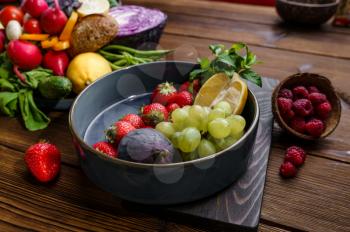 Fresh fruits and berries in plate on wooden background, corn cobs. Organic vegetarian food, grocery assortment, natural products, healthy lifestyle concept,