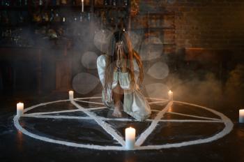Crazy demonic woman sitting in magic circle with candles, demons casting out. Exorcism, mystery paranormal ritual, dark religion, night horror, potions on shelf on background