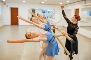 Teacher works with young ballerinas at the barre in class. Ballet school, female dancers on choreography lesson, girls practicing grace dance