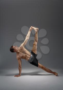Athletic yoga doing stretching exercise in studio, grey background. Strong man practicing yogi , asana training, top concentration, healthy lifestyle