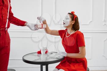 Two mime artists in red costumes, scene with gift. Pantomime theater, parody comedian, positive emotion, humour performance, funny face mimic and grimace