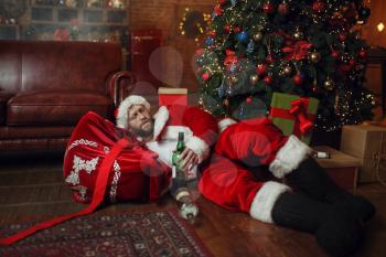 Bad drunk Santa claus sleeps under christmas tree, nasty party, humor. Unhealthy lifestyle, bearded man in holiday costume, new year and alcoholism