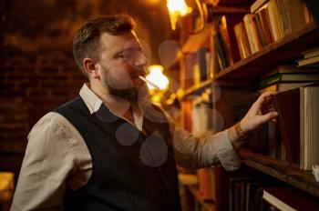 Bearded man with cigarette takes book from bookshelf and rich office interior on background. Tobacco smoking culture, specific flavor. Smoke habit