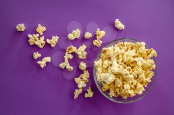 Popcorn in plate isolated on purple background, top view. Pop corn texture, tasty wallpaper design, movie or cinema food concept