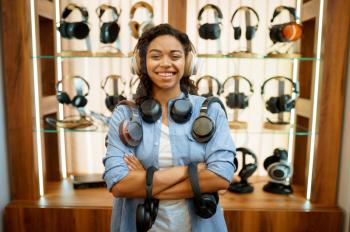 Woman with headphones in audio components store, music fan. Female person in music shop, showcase with earphones on background, buyer in multimedia salon