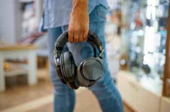 Woman buying headphones in audio store, music fan. Female person in music shop, showcase with earphones on background, buyer in multimedia salon