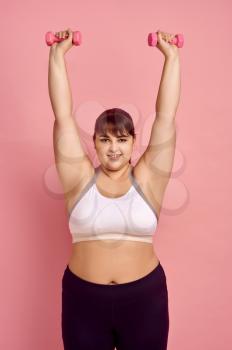 Overweight woman doing exercise with dumbbells, pink background, body positive. Obesity fighting, striving for a healthy lifestyle