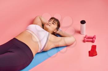 Overweight woman lying on fitness mat, body positive, pink background. Obesity fighting, striving for a healthy lifestyle