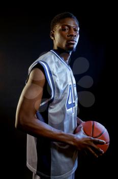 Focused basketball player holds ball in studio, black background. Professional male baller in sportswear playing sport game, tall sportsman